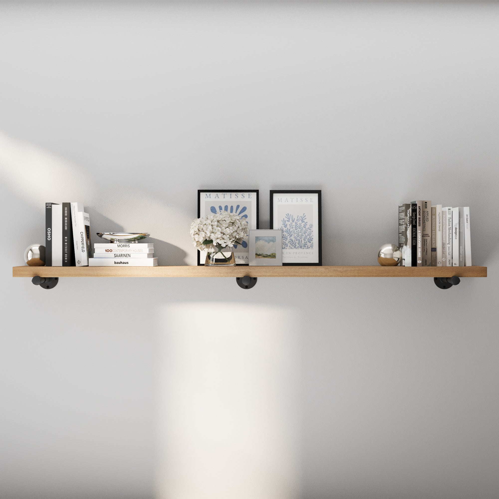 72 inch industrial pipe shelf styled in a modern interior with a warm golden oak finish and sanded wood surface. This extra long wall shelf blends rustic charm and contemporary storage for books, framed art, and living room décor.