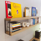 Wooden shelf with books and decor supported by black rectangular brackets in a living room.