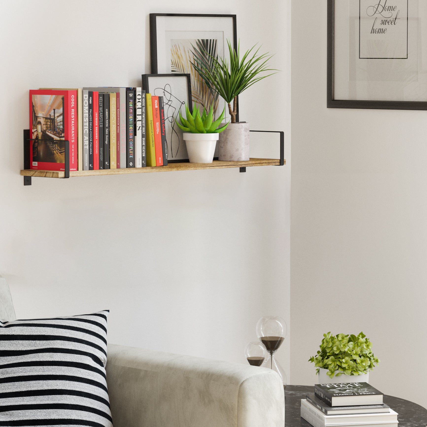 Living room decor scene with a wood shelf holding books, plants, and framed art above a gray sofa, creating a cozy corner.