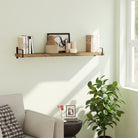 A floating shelf in a rich burnt finish with black metal side brackets mounted above a small round table and armchair. The shelf holds books, candles, and decor, offering a calming reading nook by the window.