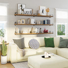 A cozy living room wall showcases three wood floating shelves styled with books, vases, and frames. These staggered shelves bring warmth and character to the modern space.