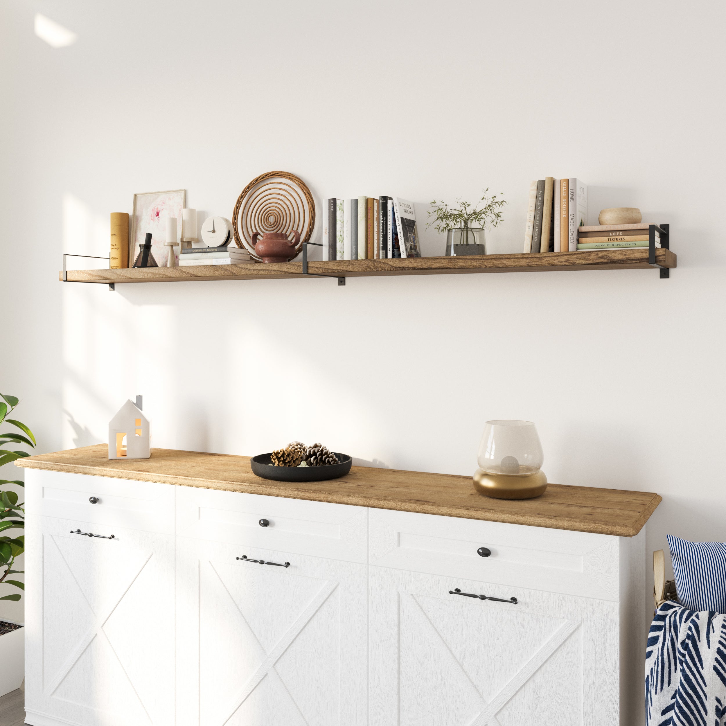 A single hanging shelf with dark brackets sits above a white farmhouse-style cabinet. It holds a mix of vases, books, and decor, blending rustic and modern for a warm, inviting touch.