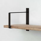  Black rectangular mounting bracket supporting a wooden shelf, mounted on a wall.