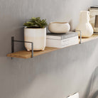 Wooden long shelf with decor items supported by black rectangular shelf brackets in a living room.