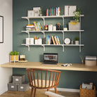 A white office shelving unit mounted above a home office desk, emphasizing its utility for organizing books, supplies, and decorative objects in workspaces.