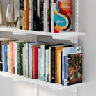 Two tiers of the floating shelf unit filled with books, highlighting the sturdy brackets and clean edge finishes of the white shelving system.
