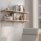 36 inch long 2 tier floating bookshelves with books and decor items against a white wall, with a chair in the foreground.