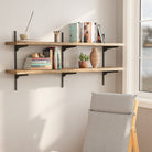 54 inch long floating bookshelf with black adjustable brackets with books and plants in a room with a chair and window.