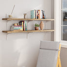 A farmhouse shelf in a rich burnt finish for living room decor with books and decor against a white wall, with a chair in the foreground.