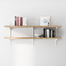 2 tier wooden adjustable shelves with white adjustable brackets with books and decor on a white wall