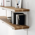 Floating bookshelf in rich burnt finish with books and decor items against a white wall