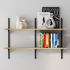 Two-tier adjustable floating wall shelf with black metal rails and light wood boards styled with books, decorative vases, and a chrome accent piece.