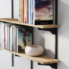 A farmhouse shelf’s wood texture and black brackets, displaying neatly organized books and a ceramic bowl for a natural, minimal aesthetic.