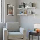 Beige armchair in a room with white floating shelves, books, and decor items.