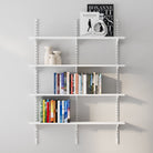 4 tier decorative shelving unit with books and decor items on a gray wall.
