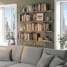 Living room book shelf with books and decor items against a wall in a living room with large windows.