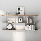 3 tiered long floating shelf with books, a clock, and decorative items against a gray wall.