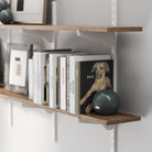 Adjustable rustic shelf with heavy duty white metal brackets and rails with books and a framed picture on a white wall