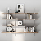 4 tiered wall mounted shelving unit with books, a clock, and decorative items against a gray wall.