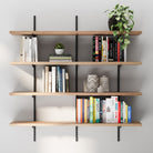 Modern interior display showing four tiered floating shelves for living room decor with black brackets and wood finish, arranged with books, plants, and decorative accents.