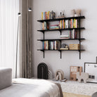 Modern bedroom scene featuring a 4-tier wall mounted black shelving unit styled with books and decor above a terrazzo bench and next to tall curtains.