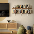 Warm living room setup with two-tier wall shelves above a console, filled with books and decor, creating a cozy and modern interior atmosphere.