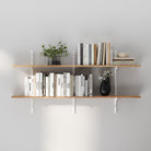 Two-tier wall shelf with white adjustable rails and brackets, styled with books and decor on a light gray wall, showcasing a clean and minimalist look.