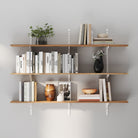 Three-tier wall shelving system with white adjustable rails and brackets, styled with books, plants, and décor on a light gray wall, offering organized and modern storage.