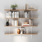 Four-tier wall shelving system with white adjustable rails and brackets, styled with books, plants, and decorative pieces on a neutral wall, offering organized and modern storage.