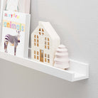 white shelf in use, featuring items like a children's book titled "My First Animals," a wooden house model, and a small decorative tree. The scene highlights the shelf’s functionality as a storage solution and its decorative potential, especially in a child’s room or a nursery, where it can organize and display books and toys neatly.